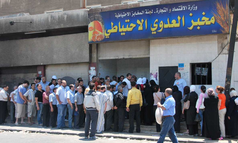 اقتصاد الندرة لجأ النظام خلال السنوات الماضية إلى محاولة الموازنة بين الاحتياجات الأساسية ونقصها، خاصة مع انهيار قيمة الليرة السورية أمام العملات الأجنبية، ودخول البلاد في أزمة اقتصادية ومعيشية حادة، مع هجرة كبيرة للسوريين باتجاه بلاد أخرى، سواء إلى الدول الأوروبية أو دول الجوار للبحث عن فرص للاستقرار الاقتصادي والمعيشي. كيف تعامل النظام مع نقص الموارد تحول الاقتصاد السوري خلال السنوات الماضية إلى “اقتصاد حرب”، أي توجيه الدولة كل طاقاتها ومواردها نحو دعم المجهود الحربي، بالتزامن مع رفع الدعم تدريجيًا وزيادة الضرائب والرسوم على السلع والخدمات. الباحث في الاقتصاد الدكتور فراس شعبو، قال لعنب بلدي، إن النظام السوري، ومع استمرار المعارك في مختلف المناطق السورية، بدأ بسحب الدعم عن الطاقة والمحروقات والأدوية والأسمدة، وكذلك عن المواد الغذائية، ووقف تأمين الاحتياجات الأساسية للعملية الإنتاجية، ما أدى إلى انخفاض حاد لدى الأخيرة، وأصبح الطلب أكبر من العرض، بالتزامن مع تدهور العملة وخروج المعامل عن الخدمة، وظهور مشكلات أمنية إضافية، وفساد داخلي. المحلل الاقتصادي يونس كريم، أوضح لعنب بلدي أن هناك إطارين للاقتصاد اتبعهما النظام في سوريا لسنوات طويلة. يتعلق الإطار الأول بتكييف المجتمع السوري على ما يُقدم له من السلع والخدمات منذ ثمانينيات القرن الـ20، وبالتالي اضطر السوريون إلى التعامل مع ندرة هذه السلع عبر تقليل احتياجهم إليها، وانتظار انخفاض سعرها، أو توفر بدائل لها أقل ثمنًا. الإطار الثاني الذي كان جزءًا من اقتصاد عالمي، يقوم على استغلال النظام القيمة التي تُعطى للسلعة ضمن مصطلح “الندرة”، فباع النفط والآثار والمعادن وحتى المعلومات حول أشخاص معينين، وأنشأ نظام دولة اقتصاديًا كاملًا يعمل لمصلحته، وهذا الإطار توقف مع اندلاع الثورة السورية. حاليًا، بحسب كريم، بقي الاقتصاد البسيط القائم على التكيف بين “الندرة” والحاجة، واستطاع السوريون التكيف وسط غياب أي حلول أخرى، إلا محاولة النظام السوري خلق اقتصاد موازٍ للسلع والخدمات عن طريق الدوائر المقربة منه. فراس شعبو أشار إلى أن النظام السوري تعامل مع الاقتصاد من مبدأ وجوب استمرار كيان الدولة لا مؤسساتها الاقتصادية، فهو لا يهتم بتحسين الأوضاع الاقتصادية أو إنشاء مشاريع حقيقية لتحسين دخل المواطنين، بقدر ما يتبع خطوات تضمن استمراريته، وهو ما سينعكس على تطور سوريا مستقبلًا. وفي تقرير “البنك الدولي” لممارسة الأعمال، الصادر في عام 2020، حلّت سوريا في المرتبة 176 من أصل 190 دولة، وبالمرتبة 143 في بدء النشاطات التجارية، و186 في استخراج تراخيص البناء. ما “اقتصاد الندرة”؟ لا يوجد في علم الاقتصاد مصطلح يدعى “اقتصاد الندرة”، لكن العلم يدرس كيفية مواءمة الموارد مع الاحتياجات والفجوة بينهما، ومن هنا نشأ المصطلح، على اعتبار أن احتياجات الإنسان أكبر من موارده، لأنها متكررة ومتجددة بعكس الموارد المحدودة، ومن هنا تأتي “الندرة”، لسوء استغلال أو استخدام أو نفاد بعض الموارد، وفق الباحث في الاقتصاد الدكتور فراس شعبو. المحلل الاقتصادي يونس كريم قال لعنب بلدي، إنه كلما زادت ندرة السلعة وزاد الاحتياج إليها، ارتفع سعرها، وفي هذه الحالة تعتبر الندرة “أمرًا نسبيًا”. كريم أشار إلى أنه في الظروف الطبيعية أصبح مصطلح “الندرة” ضعيفًا نتيجة الأسواق المفتوحة، ما نقل “الندرة” لتصبح عمودًا فقريًا للأرباح في بلاد فيها الموارد أكبر من الاحتياجات، كدول الخليج على سبيل المثال. تأثيرات سلبية مستقبلية في 21 من حزيران الماضي، قال مبعوث الاتحاد الأوروبي إلى سوريا، دان ستوينيسكو، في تغريدة عبر حسابه في “تويتر“، إن تسعة من كل عشرة سوريين يريدون مغادرة البلاد، ولدى كل خمسة منهم خطط ملموسة، وأربعة منهم يتعلمون اللغة الألمانية. تعكس هذه التغريدة الرغبة الواضحة لدى شريحة واسعة من السوريين بمغادرة سوريا إلى دول أخرى، كنتيجة للظروف الاقتصادية الحالية، التي تدفع السوريين للبحث عن خيارات أفضل، وإيجاد حلول أمام أزمة اقتصادية كبيرة. تتمثل الأزمة الحالية بارتفاع كبير بأسعار المواد الغذائية والفواكه والخضار، مع انخفاض قيمة العملة أمام الدولار الأمريكي، وسحب النظام الدعم على السلع والطاقة لشرائح واسعة من السوريين، وتحديد الدعم لشرائح أخرى ضمن آلية استحدثها في عام 2018، أطلق عليها اسم “البطاقة الذكية”. وكانت مخصصات مادة البنزين أولى المواد التي ألحقت بالبطاقة، ثم المازوت والغاز وعديد من المواد الغذائية، مع تحديد لمخصصات العائلة السورية منها شهريًا، تحت عنوان “ترشيد استهلاك المخصصات”. الباحث في الاقتصاد الدكتور فراس شعبو، قال لعنب بلدي، إن المحرك الأساس لأي اقتصاد هو الموارد البشرية، والأزمات الاقتصادية الأخيرة وتفريغ موارد الدولة باتجاه المجهود الحربي أدت إلى تفريغ سوريا من العمالة وهجرة العقول والشباب، ما يعني أن البلاد أصبحت عاجزة. شعبو أوضح أنه لو جاءت الأموال الدولية لدعم الاقتصاد، لن تكون هناك نتيجة إيجابية جراء الهجرة المتزايدة. وفي المقابل، التحركات الاقتصادية التي اتبعها النظام السوري، بما فيها التحايل على الاقتصاد الأساسي أو النظامي، وتدميره مع خلق أسواق موازية (الأسواق السوداء)، وسيادة السلب والابتزاز والاستغلال، والعمل على السيطرة على مفاصل الاقتصاد، دمرت الأخير بشكل كبير. يبلغ سعر صرف الدولار الأمريكي الواحد حوالي تسعة آلاف ليرة سورية، وفق موقع “الليرة اليوم” المتخصص بأسعار صرف العملات. وتصدّر السوريون قائمة الجنسيات الأكبر عددًا في طلبات اللجوء المقدمة بدول الاتحاد الأوروبي، وبلغت 132 ألف طلب قدمها سوريون لعام 2022، وفقًا لأرقام “وكالة اللجوء” (EUAA) التابعة للاتحاد الأوروبي. ووفق “مفوضية اللاجئين”، تجاوزت أعداد اللاجئين السوريين الذين يعيشون حول العالم 5.5 مليون شخص، بينما وصلت أعداد النازحين داخليًا إلى نحو 6.8 مليون شخص. المحلل الاقتصادي يونس الكريم، أشار في حديثه لعنب بلدي إلى أن أي تأثير سلبي أو إيجابي عمومًا، يعتمد على الشكل الاقتصادي للدولة. وتابع أنه في النظام الاقتصادي الحر، تعتبر “الندرة” هي العمود الفقري للأرباح، وتعطي قيمة للإنتاج والخطط المستقبلية، ودونها لا معنى لعملية الإنتاج والتخطيط الاقتصادي.